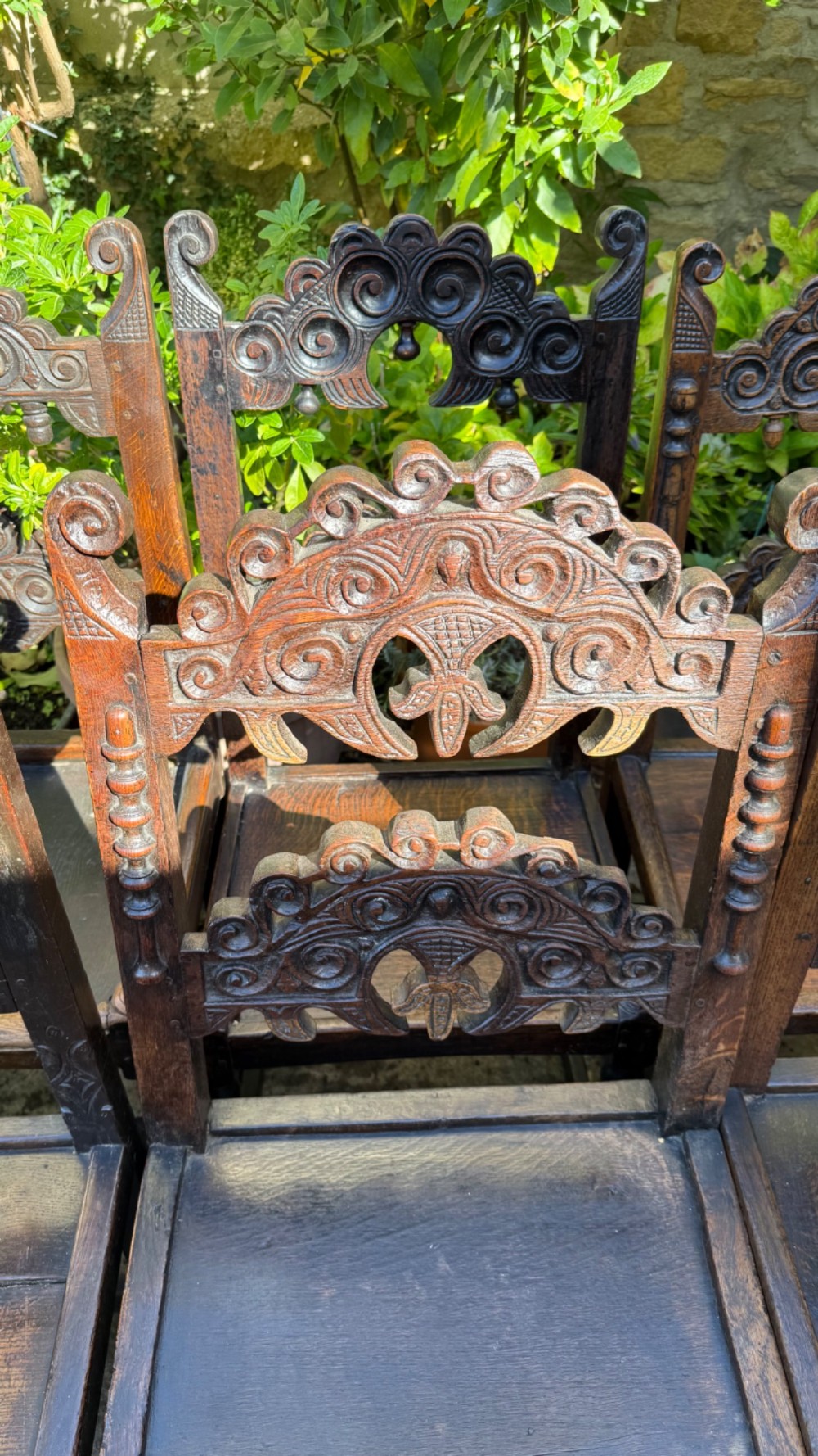 A set of dark carved oak dining chairs featuring carved openwork backs with scroll motifs, solid wooden seats, and turned front legs. View XIV