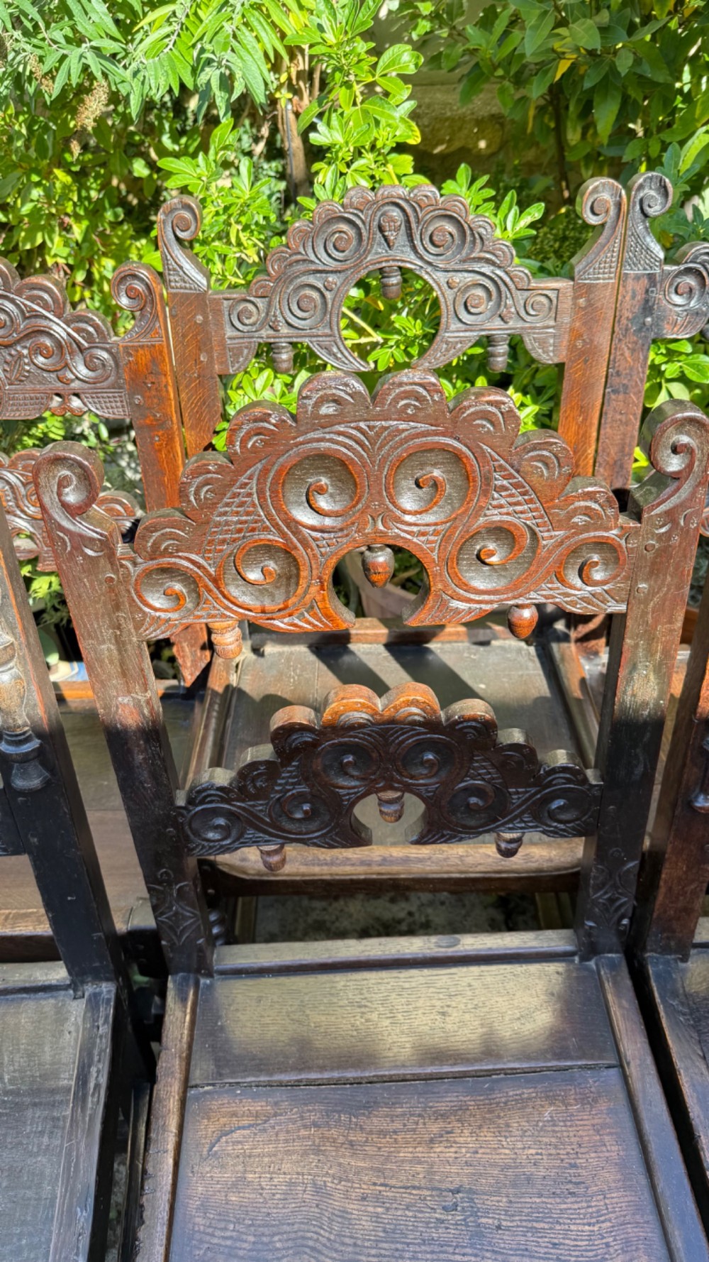 A set of dark carved oak dining chairs featuring carved openwork backs with scroll motifs, solid wooden seats, and turned front legs. View XV