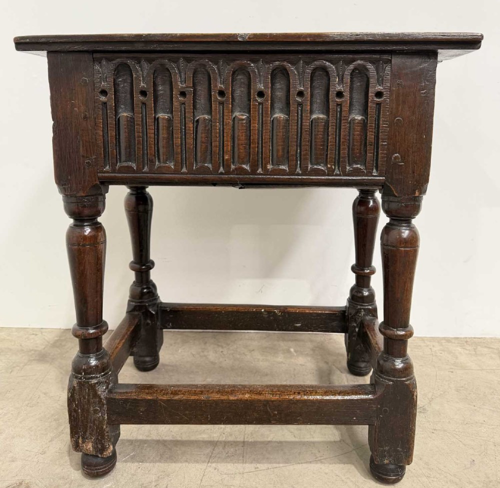 A 17th-century dark oak joint stool featuring a carved arcade frieze, turned legs, and sturdy base stretchers.