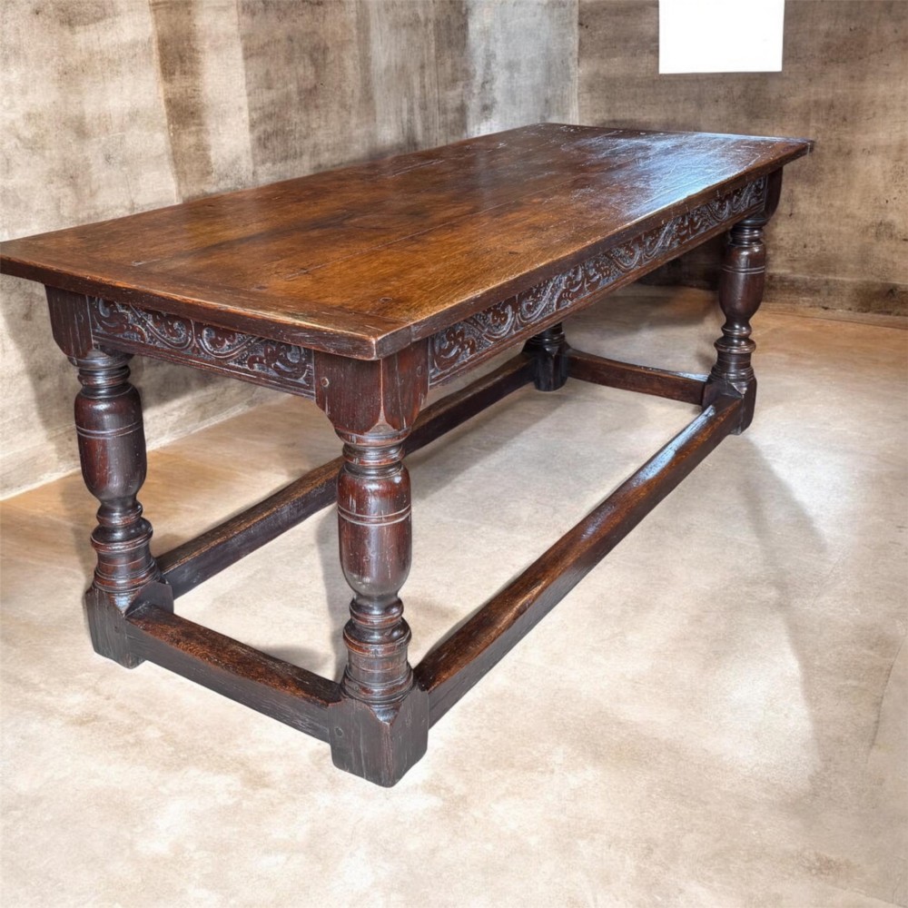 A 17th-century dark oak refectory dining table featuring a carved decorative frieze, turned baluster legs, and low perimeter stretchers.