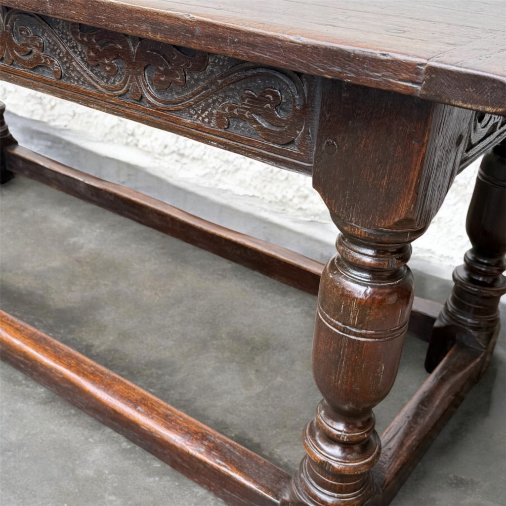 A 17th-century dark oak refectory dining table featuring a carved decorative frieze, turned baluster legs, and low perimeter stretchers. View V