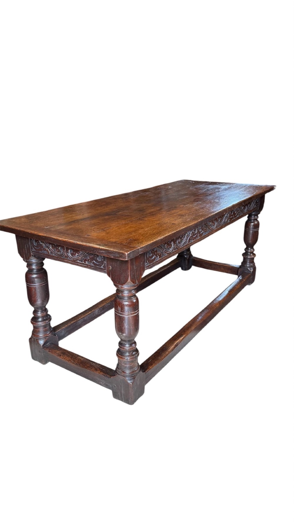 A 17th-century dark oak refectory dining table featuring a carved decorative frieze, turned baluster legs, and low perimeter stretchers. View VI