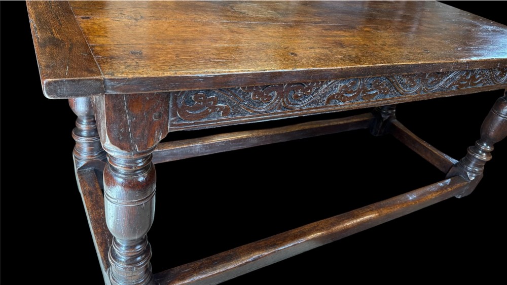 A 17th-century dark oak refectory dining table featuring a carved decorative frieze, turned baluster legs, and low perimeter stretchers. View VII