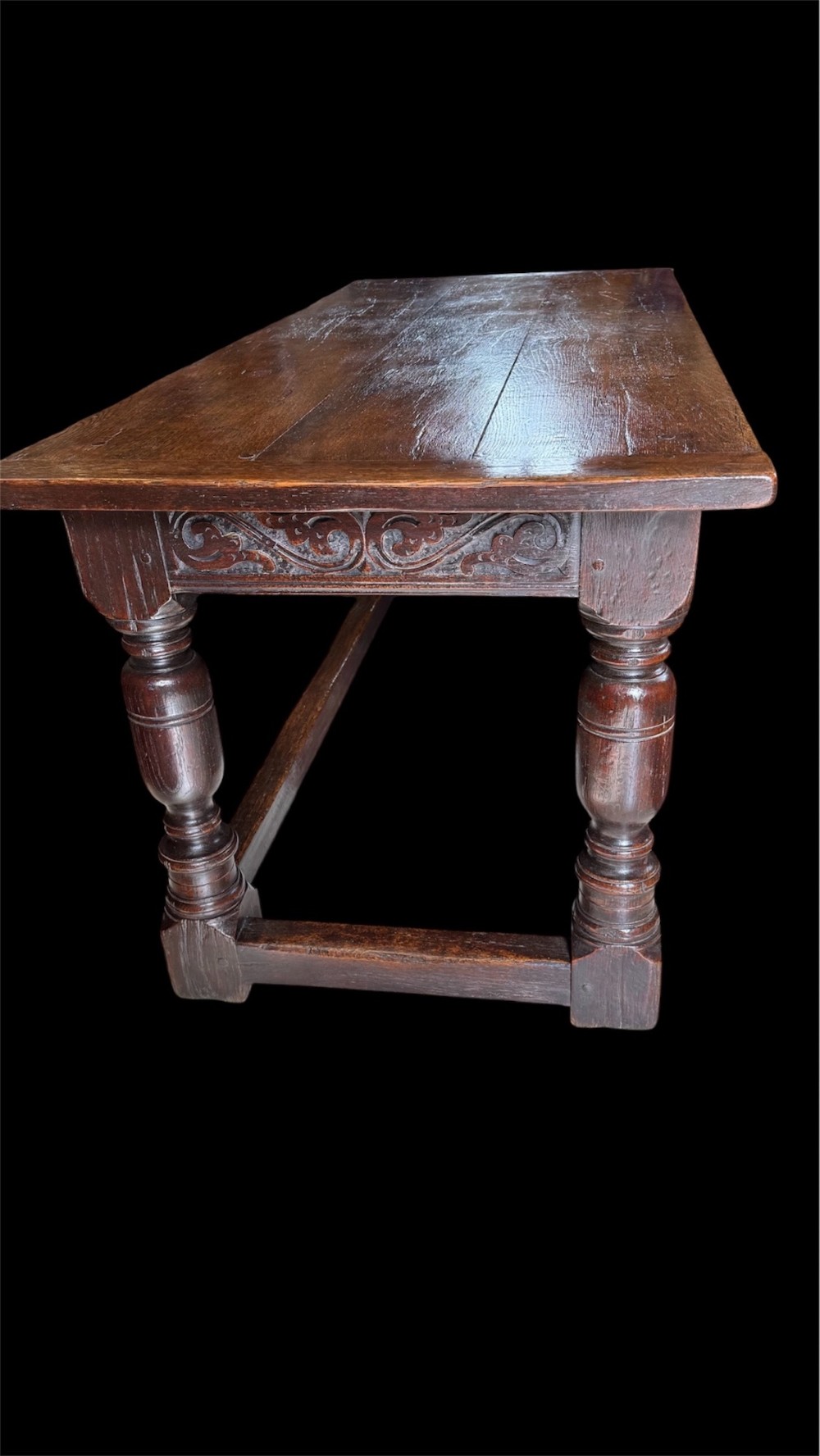 A 17th-century dark oak refectory dining table featuring a carved decorative frieze, turned baluster legs, and low perimeter stretchers. View VIII