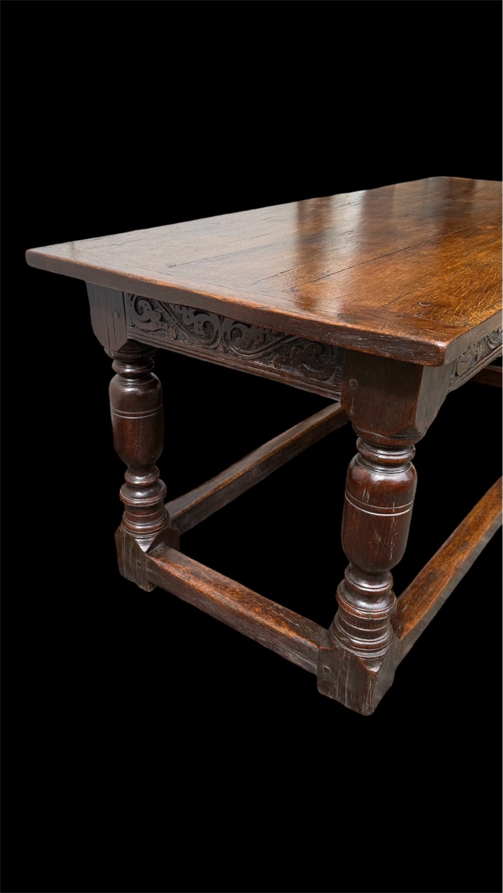 A 17th-century dark oak refectory dining table featuring a carved decorative frieze, turned baluster legs, and low perimeter stretchers. View X