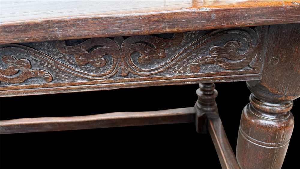 A 17th-century dark oak refectory dining table featuring a carved decorative frieze, turned baluster legs, and low perimeter stretchers. View XI