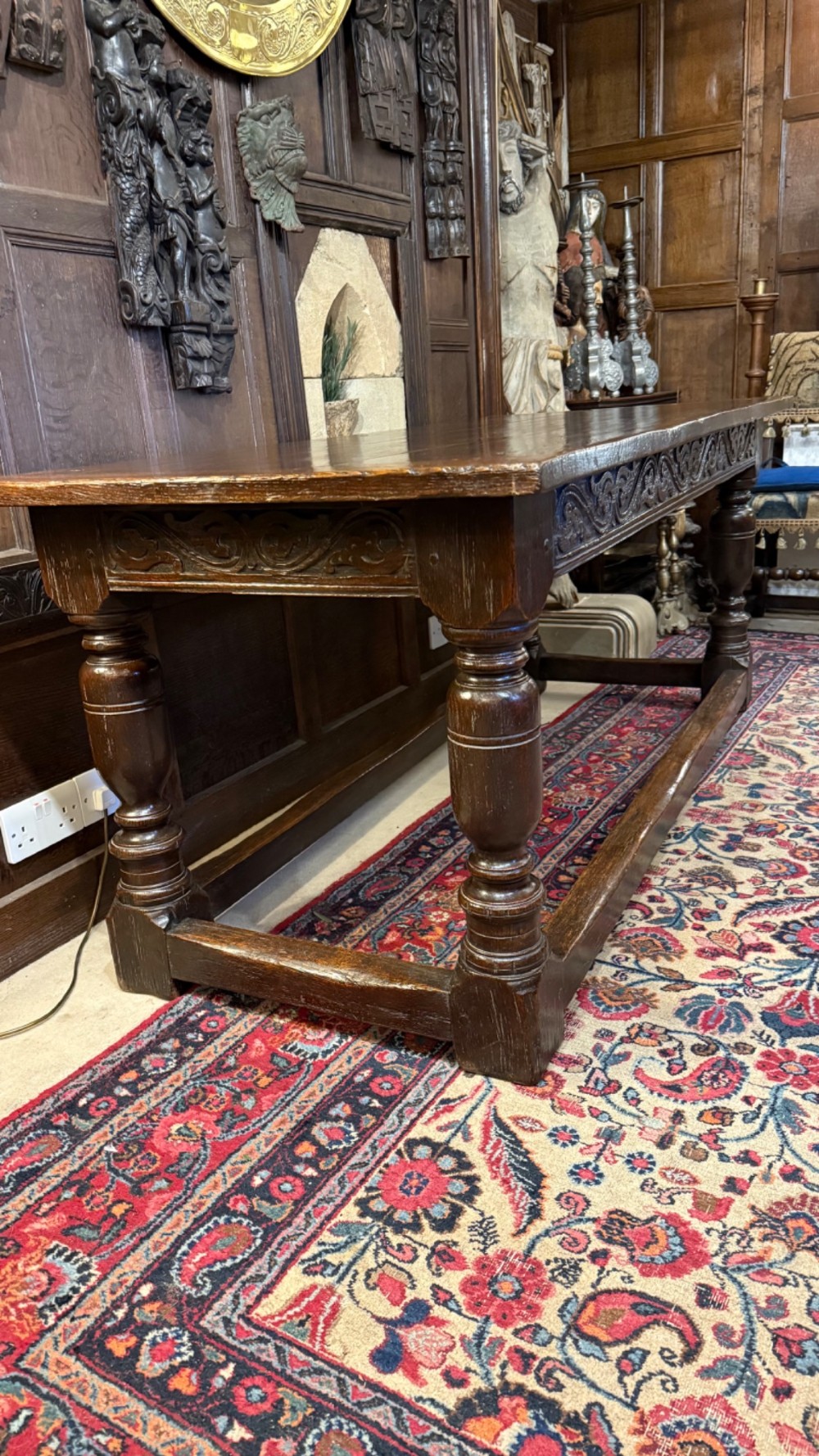 A 17th-century dark oak refectory dining table featuring a carved decorative frieze, turned baluster legs, and low perimeter stretchers. View XII
