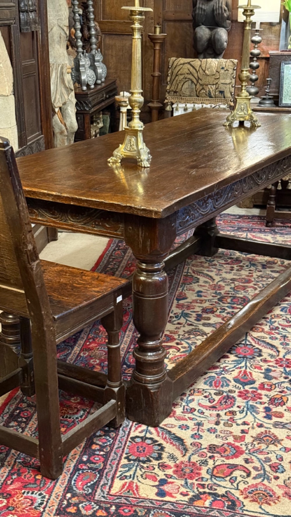 A 17th-century dark oak refectory dining table featuring a carved decorative frieze, turned baluster legs, and low perimeter stretchers. View XV