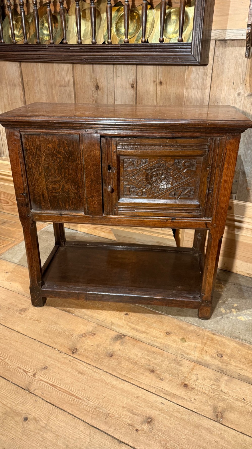 A 17th-century dark oak livery cupboard featuring a single door carved with initials and dated 1674, supported on upright legs with an open lower shelf.