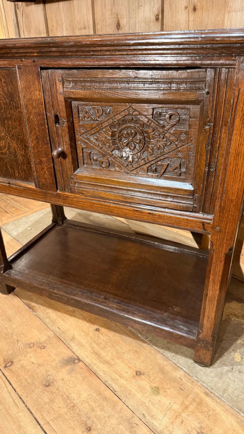 A 17th-century dark oak livery cupboard featuring a single door carved with initials and dated 1674, supported on upright legs with an open lower shelf. View II