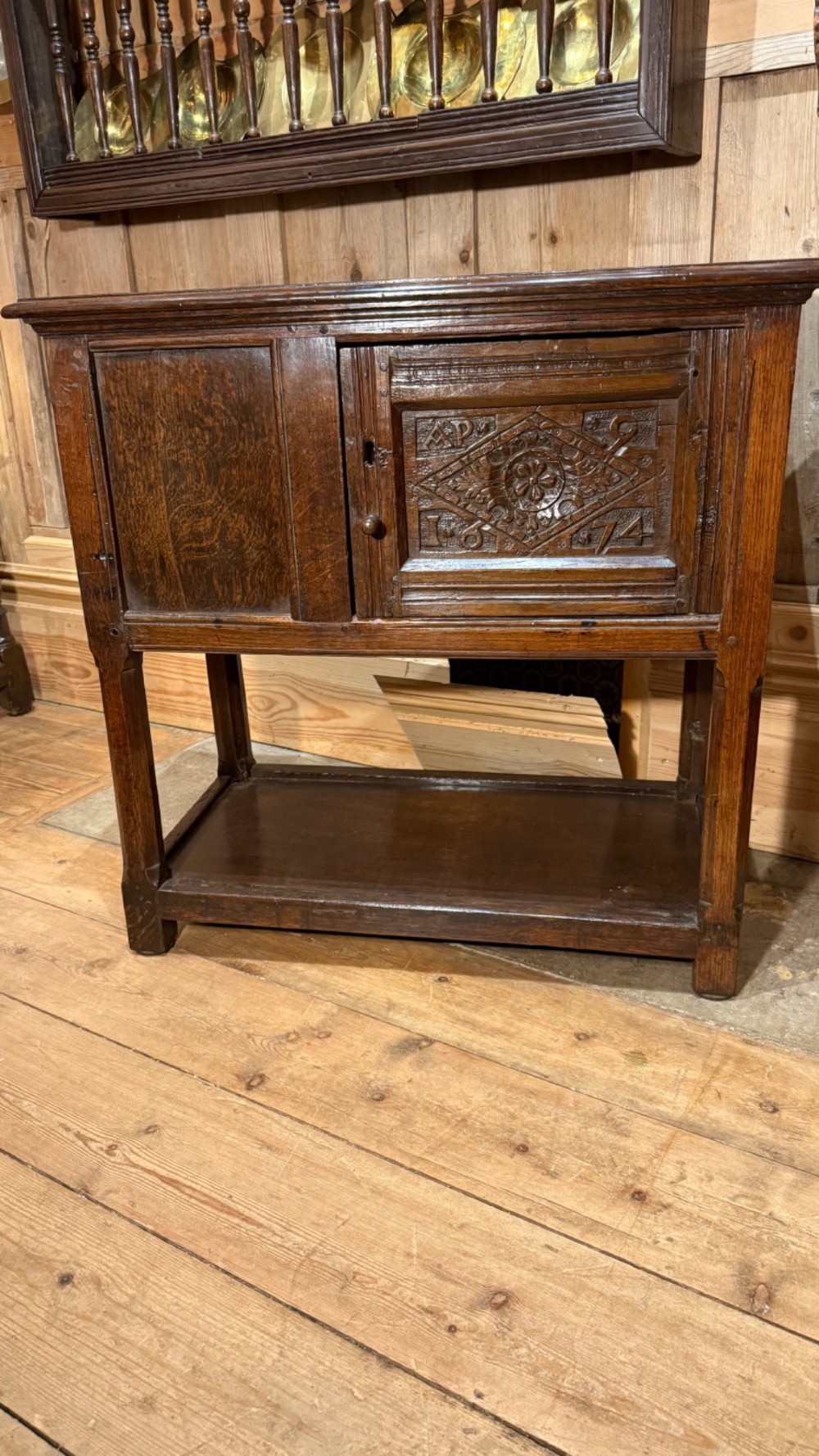A 17th-century dark oak livery cupboard featuring a single door carved with initials and dated 1674, supported on upright legs with an open lower shelf. View IV