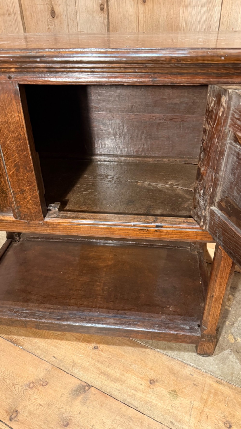A 17th-century dark oak livery cupboard featuring a single door carved with initials and dated 1674, supported on upright legs with an open lower shelf. View VII