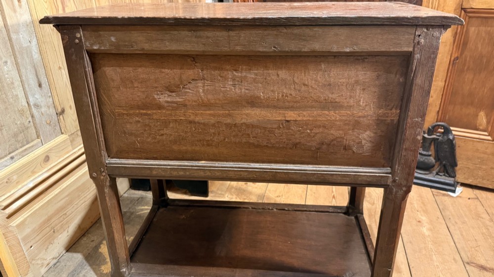 A 17th-century dark oak livery cupboard featuring a single door carved with initials and dated 1674, supported on upright legs with an open lower shelf. View XII
