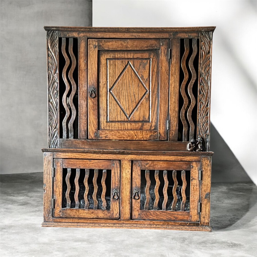 An 18th-century carved oak wall cabinet featuring a central door with a carved diamond motif flanked by wavy vertical slats and a lower two-door slatted cupboard.