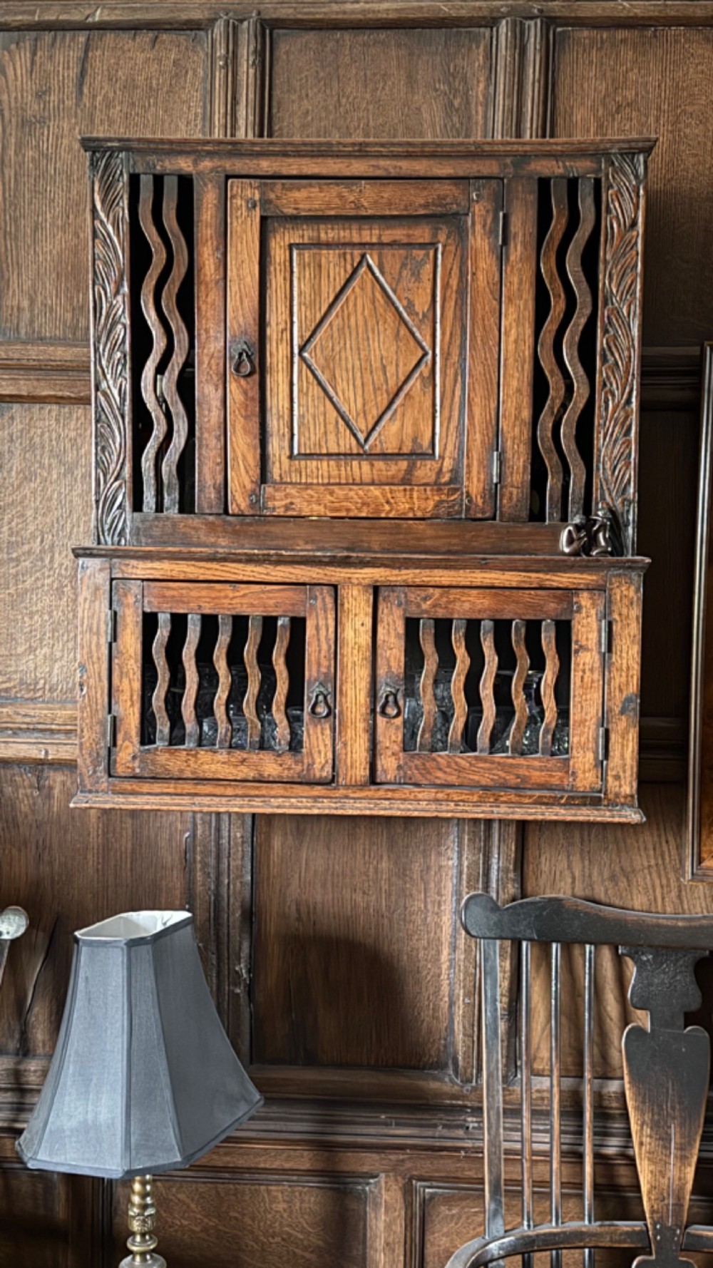 An 18th-century carved oak wall cabinet featuring a central door with a carved diamond motif flanked by wavy vertical slats and a lower two-door slatted cupboard. View III