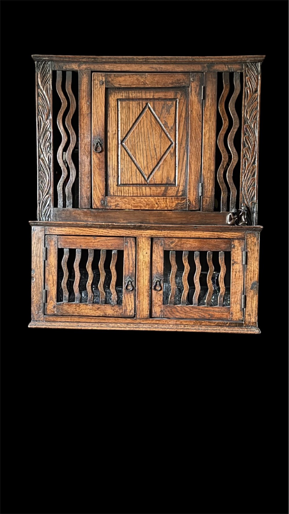 An 18th-century carved oak wall cabinet featuring a central door with a carved diamond motif flanked by wavy vertical slats and a lower two-door slatted cupboard. View IV