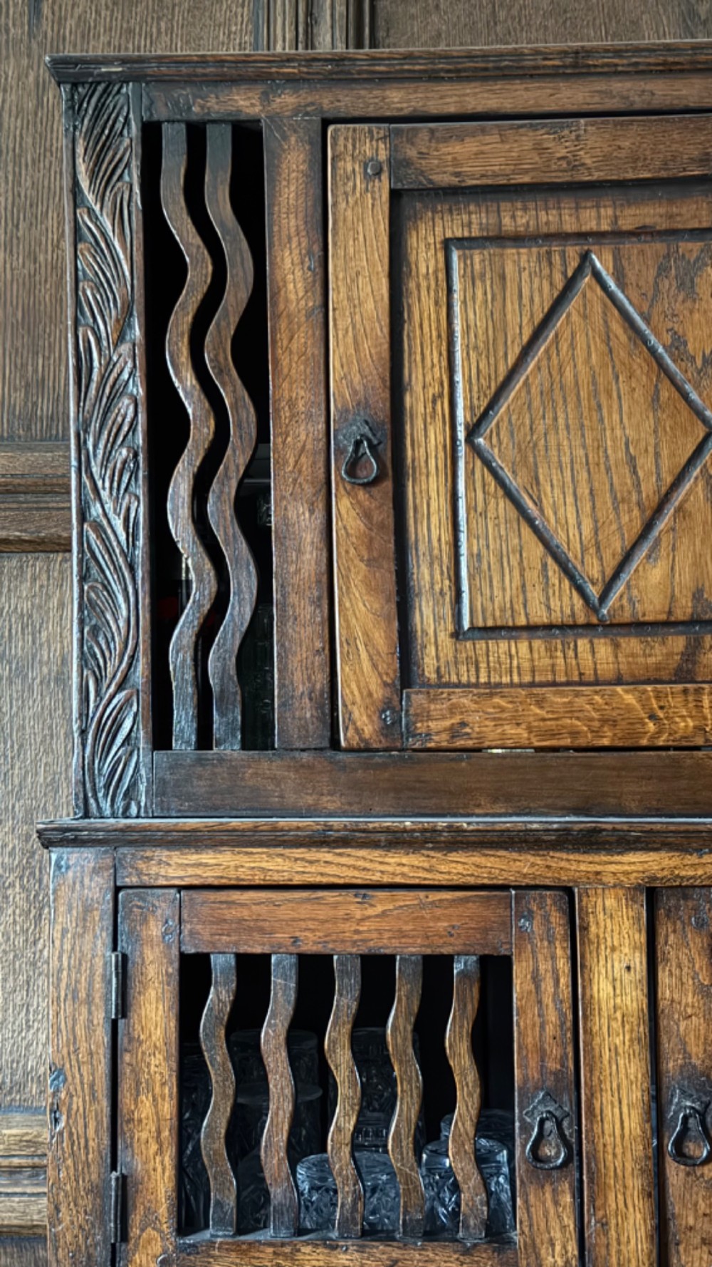 An 18th-century carved oak wall cabinet featuring a central door with a carved diamond motif flanked by wavy vertical slats and a lower two-door slatted cupboard. View V