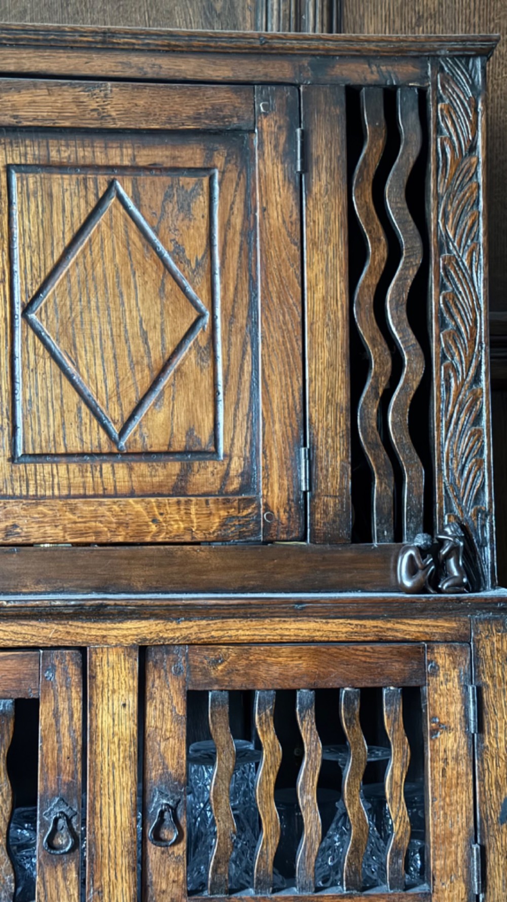 An 18th-century carved oak wall cabinet featuring a central door with a carved diamond motif flanked by wavy vertical slats and a lower two-door slatted cupboard. View VI