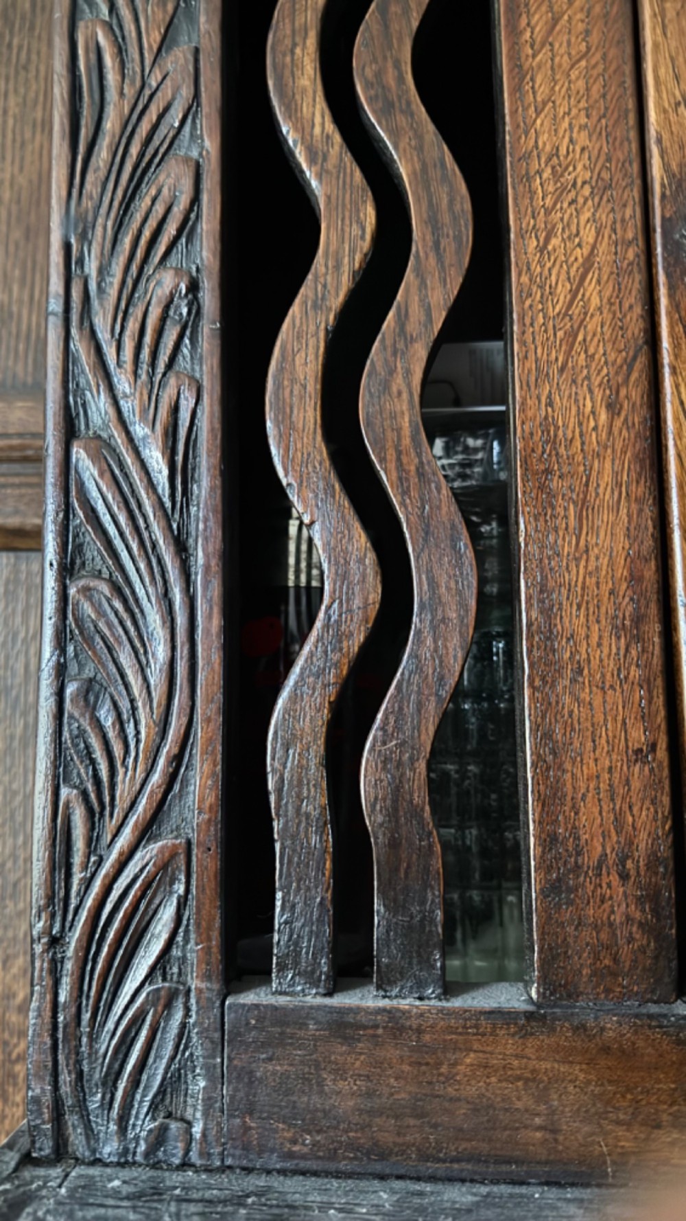 An 18th-century carved oak wall cabinet featuring a central door with a carved diamond motif flanked by wavy vertical slats and a lower two-door slatted cupboard. View VII