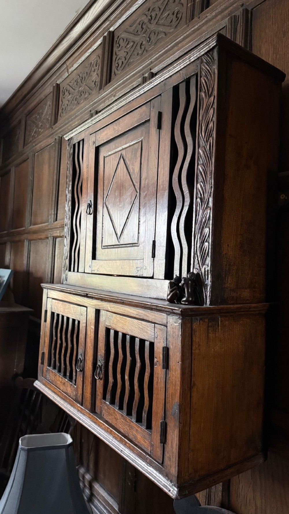 An 18th-century carved oak wall cabinet featuring a central door with a carved diamond motif flanked by wavy vertical slats and a lower two-door slatted cupboard. View VIII