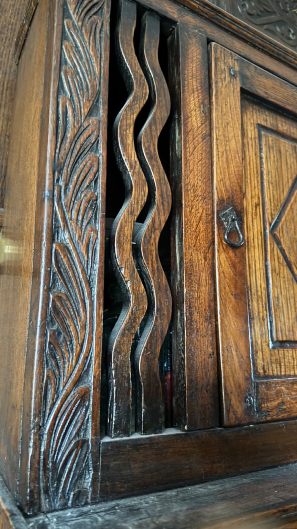 An 18th-century carved oak wall cabinet featuring a central door with a carved diamond motif flanked by wavy vertical slats and a lower two-door slatted cupboard. View IX