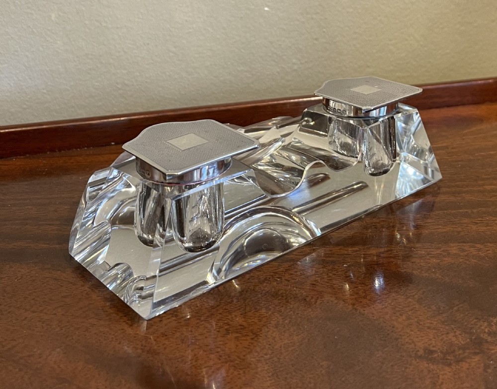 A clear cut glass inkstand featuring two square well compartments with engine-turned silver hinged lids and carved pen rests. View III