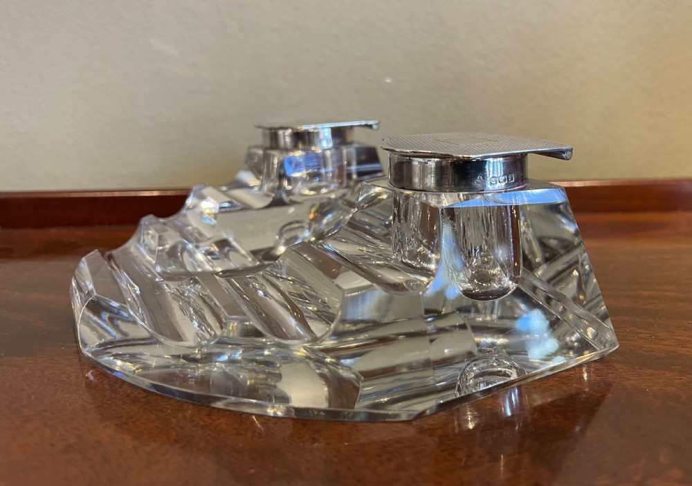 A clear cut glass inkstand featuring two square well compartments with engine-turned silver hinged lids and carved pen rests. View V