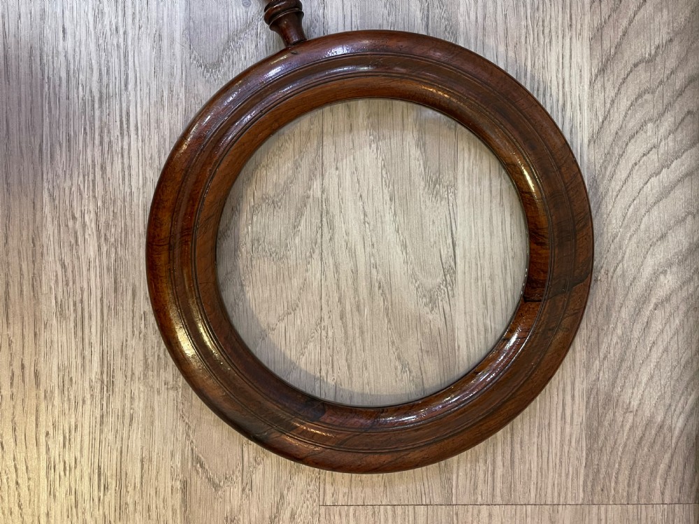 A large Regency rosewood hand held magnifying gallery glass. The glass lens surrounded by a circular border and turned handle.  View III