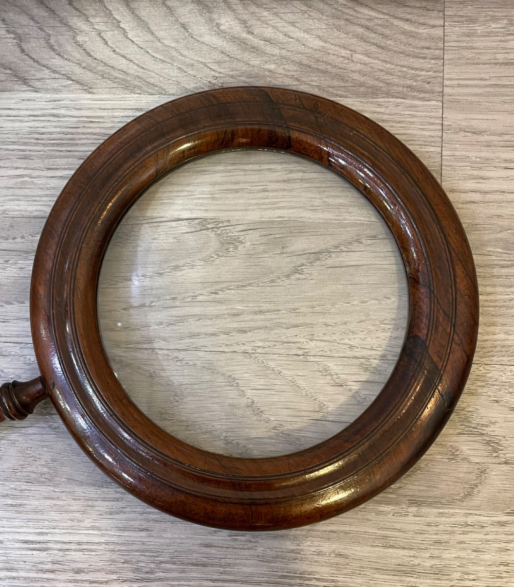 A large Regency rosewood hand held magnifying gallery glass. The glass lens surrounded by a circular border and turned handle.  View IV