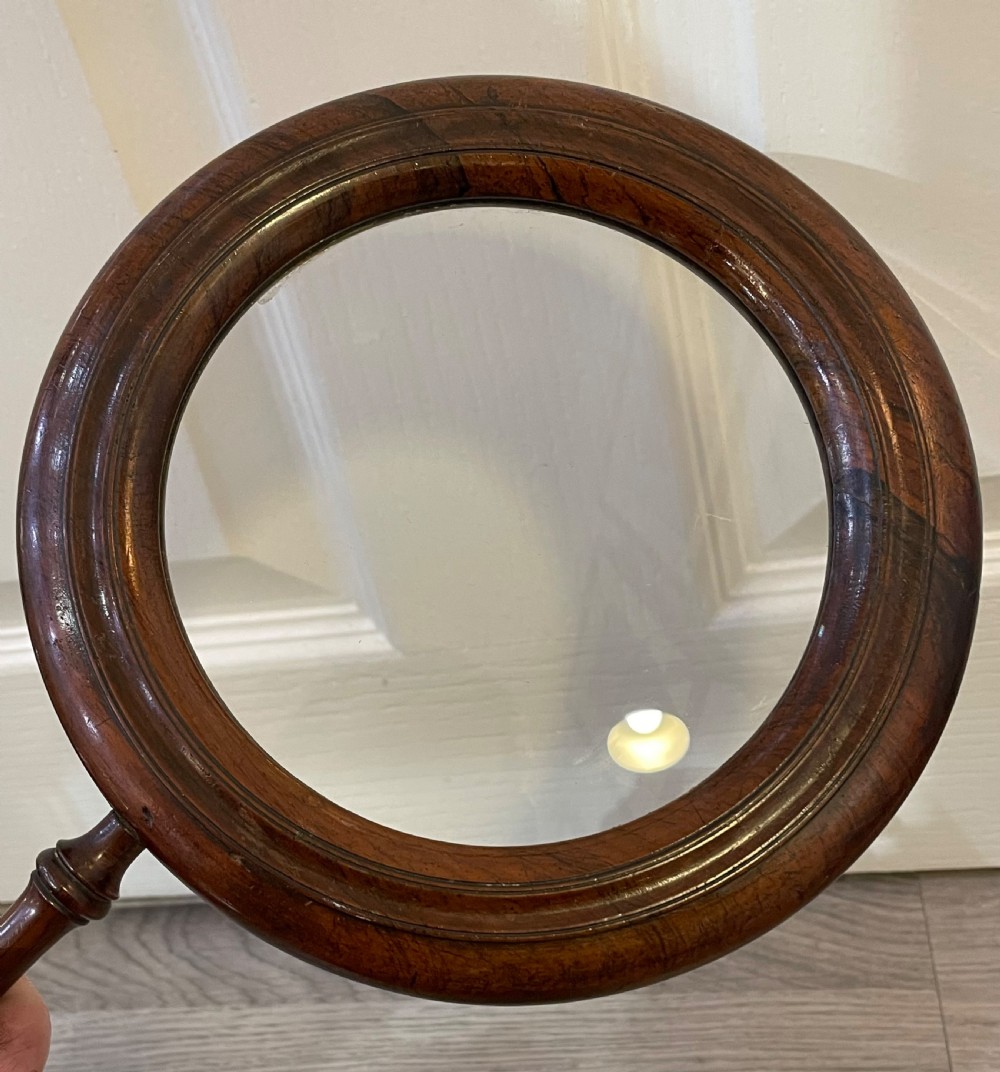 A large Regency rosewood hand held magnifying gallery glass. The glass lens surrounded by a circular border and turned handle.  View VI