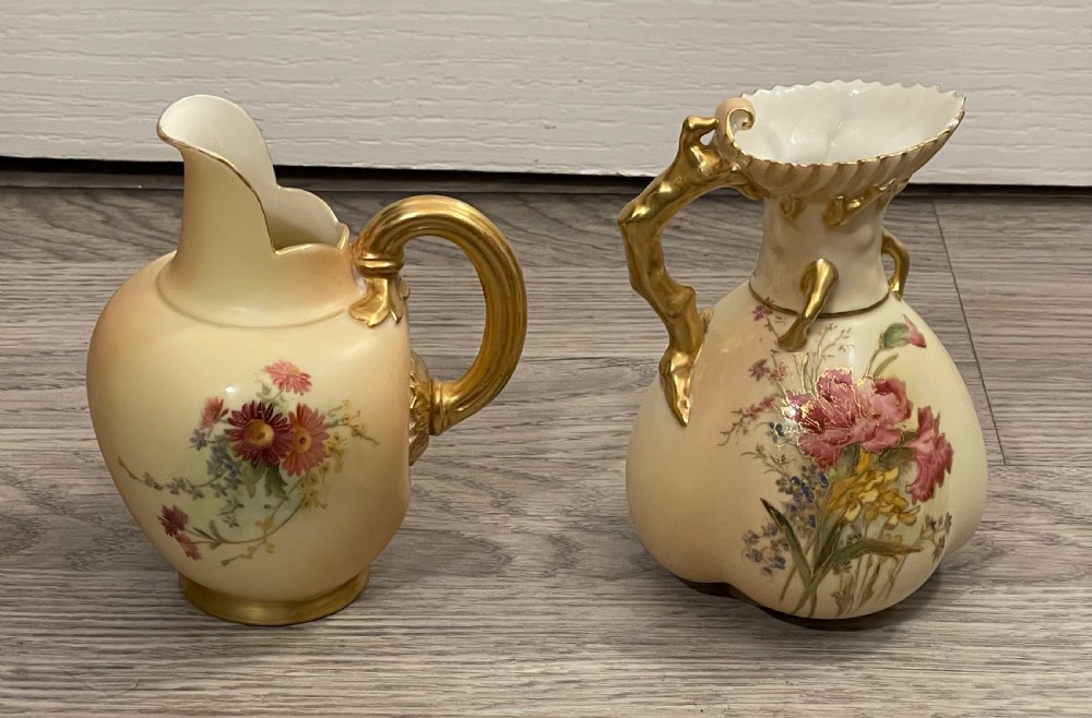 A pair of Victorian Royal Worcester porcelain jugs featuring a blush ivory ground, hand-painted floral sprays, and gilded handles.