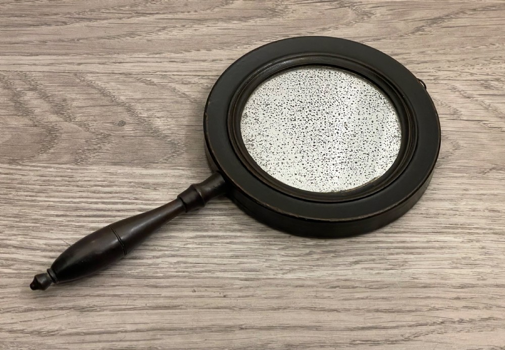 A circular double-sided Regency hand-held mirror featuring an ebonised turned wooden handle and original foxed glass plate. View III