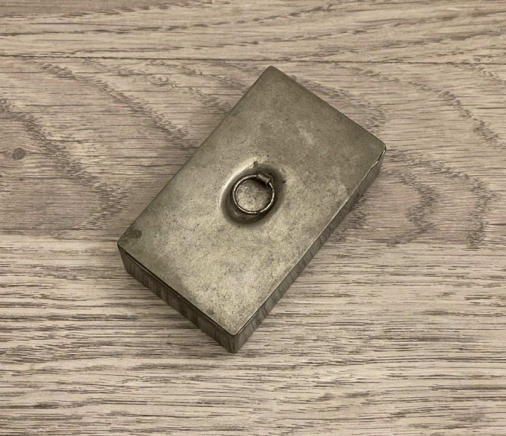 A rectangular 19th-century pewter snuff box featuring a flat hinged lid with a central recessed ring pull handle. View V