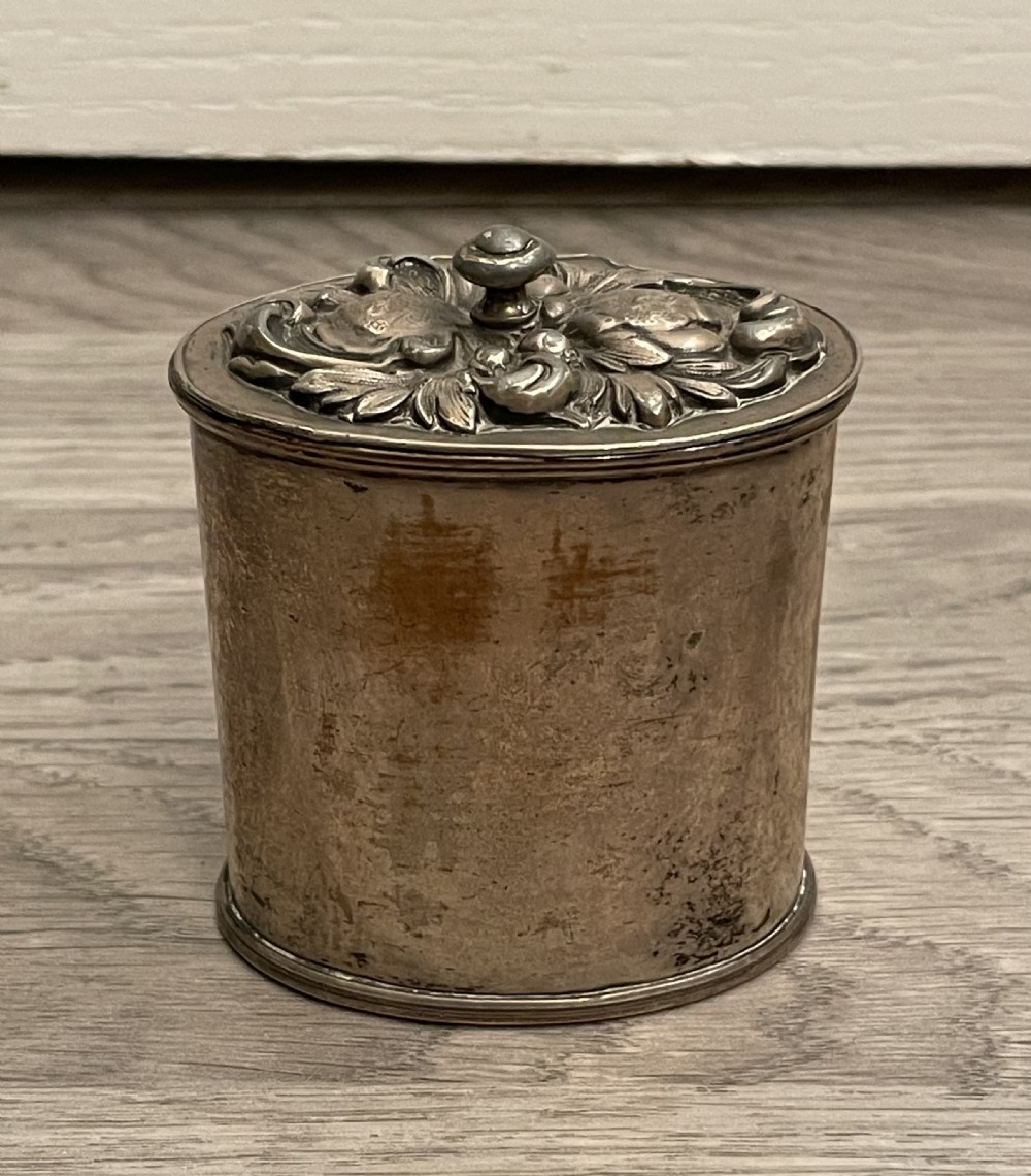 A cylindrical silver plated tea caddy featuring a repousse foliate patterned lid with a raised central finial.