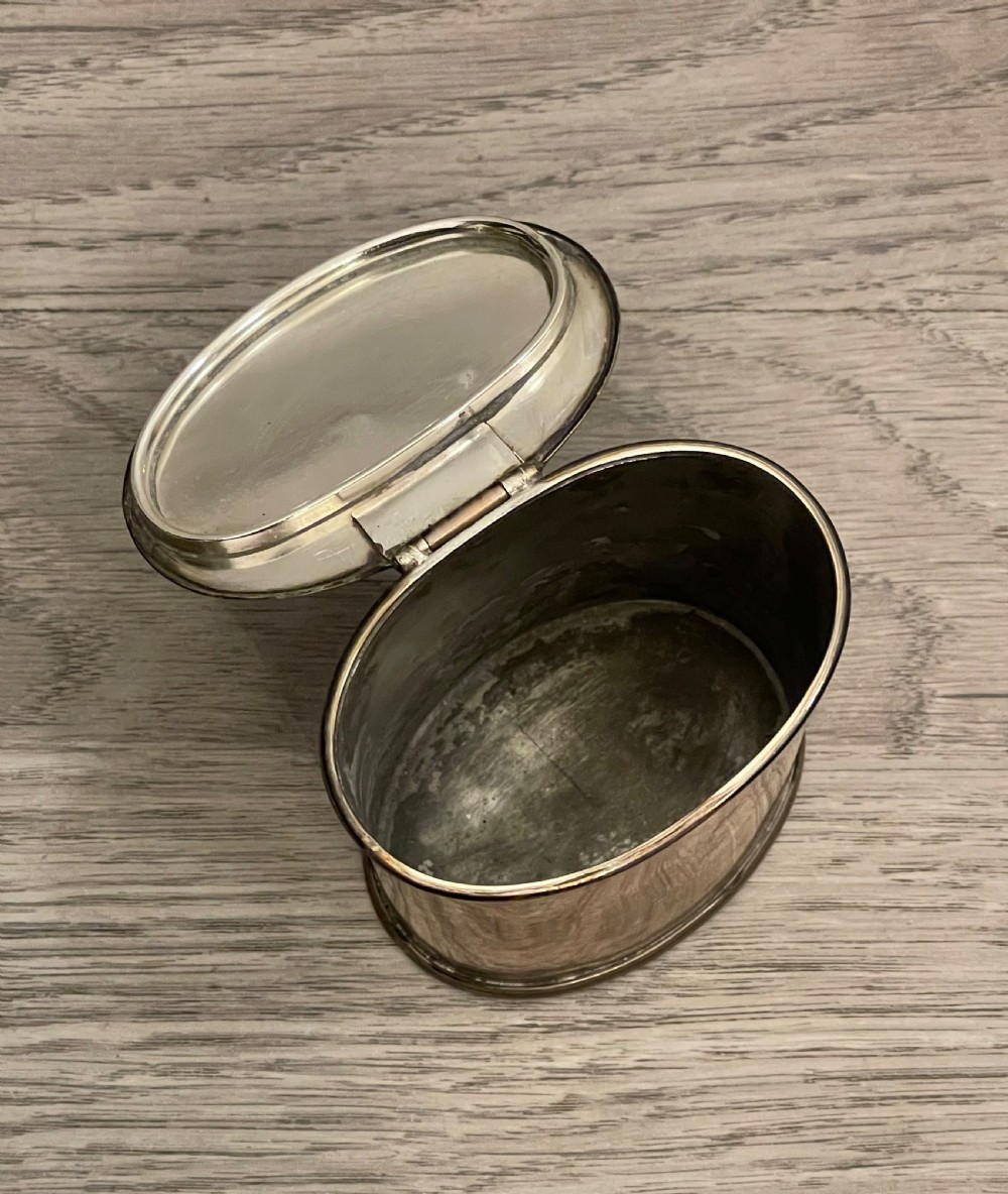 A cylindrical silver plated tea caddy featuring a repousse foliate patterned lid with a raised central finial. View III