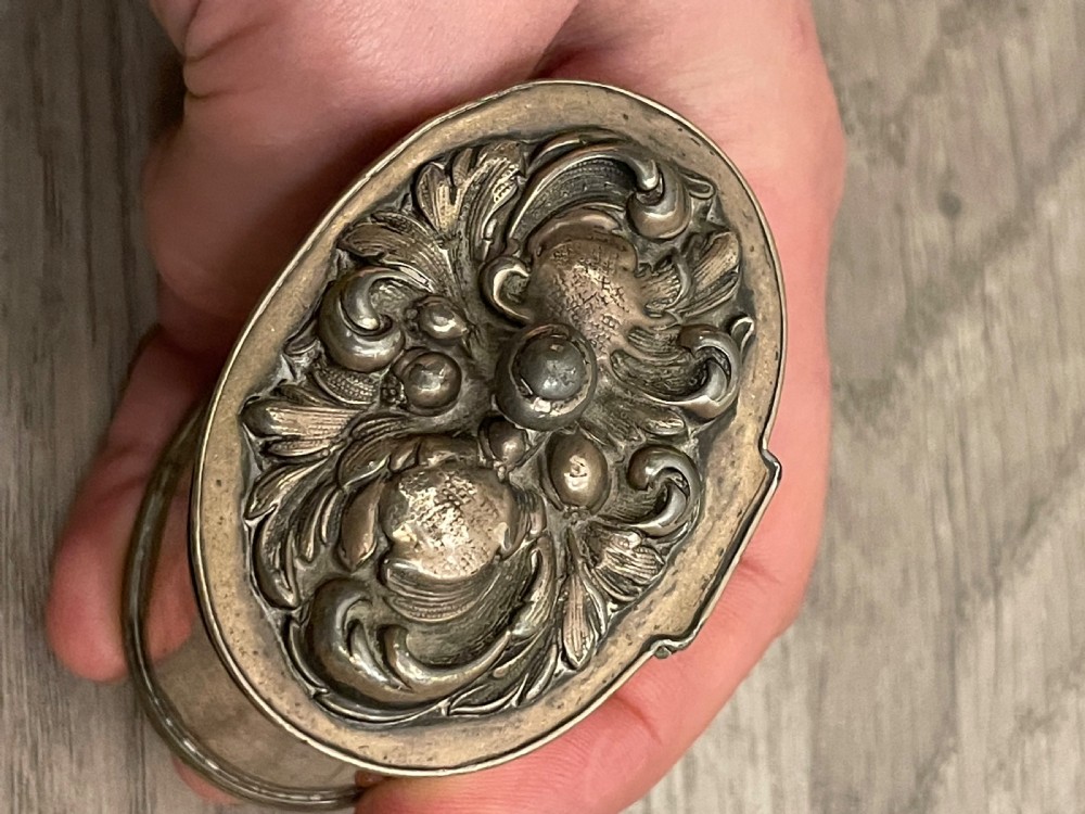 A cylindrical silver plated tea caddy featuring a repousse foliate patterned lid with a raised central finial. View IV