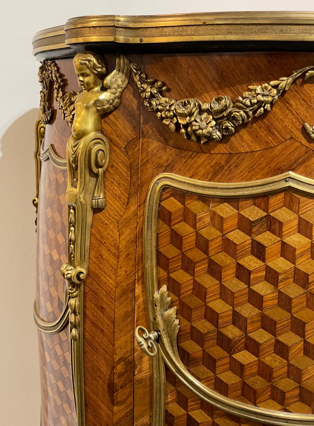 A French kingwood bedside cabinet featuring cube parquetry inlay, gilt ormolu mounts, floral garlands, and a shaped marble top. View VII