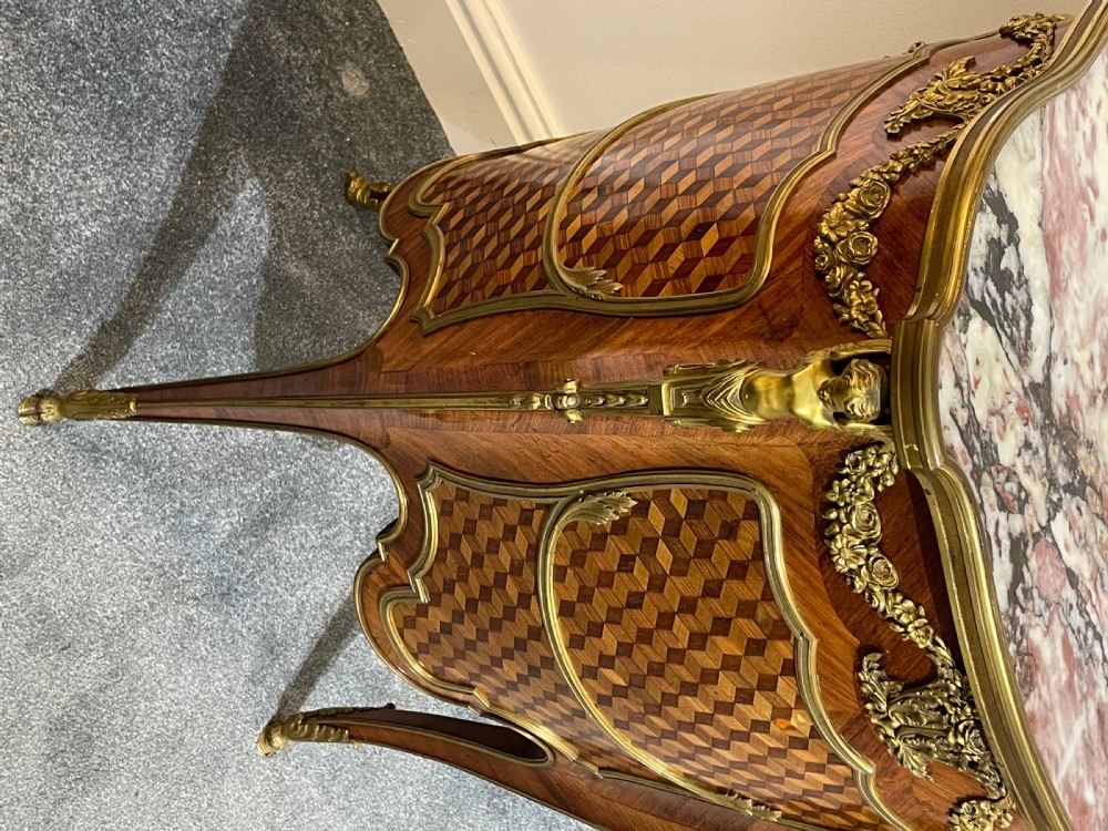 A French kingwood bedside cabinet featuring cube parquetry inlay, gilt ormolu mounts, floral garlands, and a shaped marble top. View IX