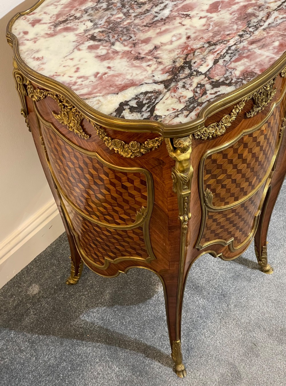 A French kingwood bedside cabinet featuring cube parquetry inlay, gilt ormolu mounts, floral garlands, and a shaped marble top. View XI