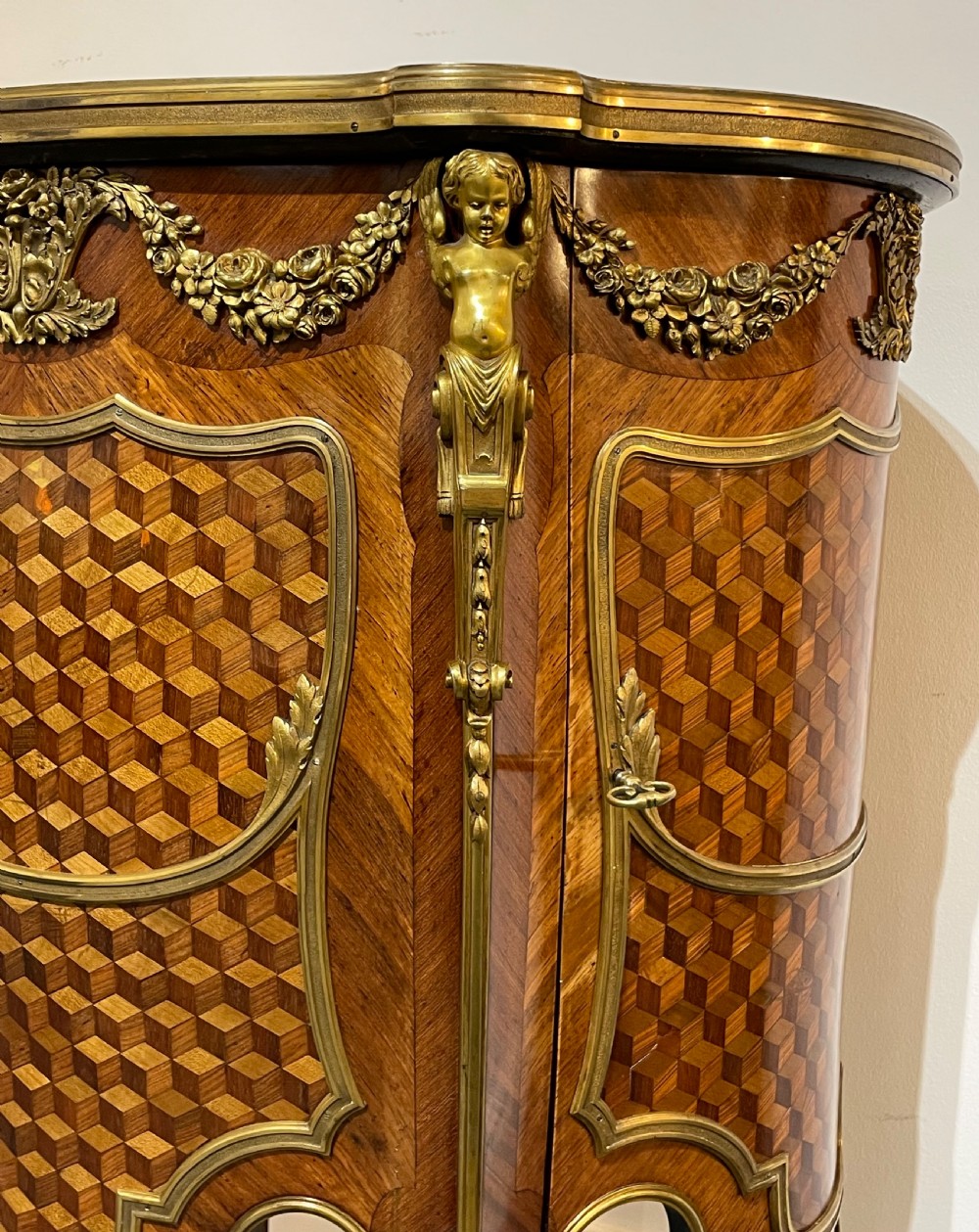 A French kingwood bedside cabinet featuring cube parquetry inlay, gilt ormolu mounts, floral garlands, and a shaped marble top. View XIV