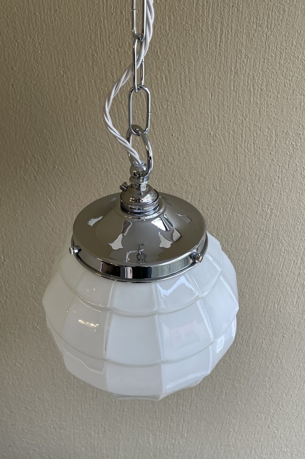 A white opaline glass spherical pendant light with a moulded fish scale texture, suspended by a chrome gallery and metal chain. View IV