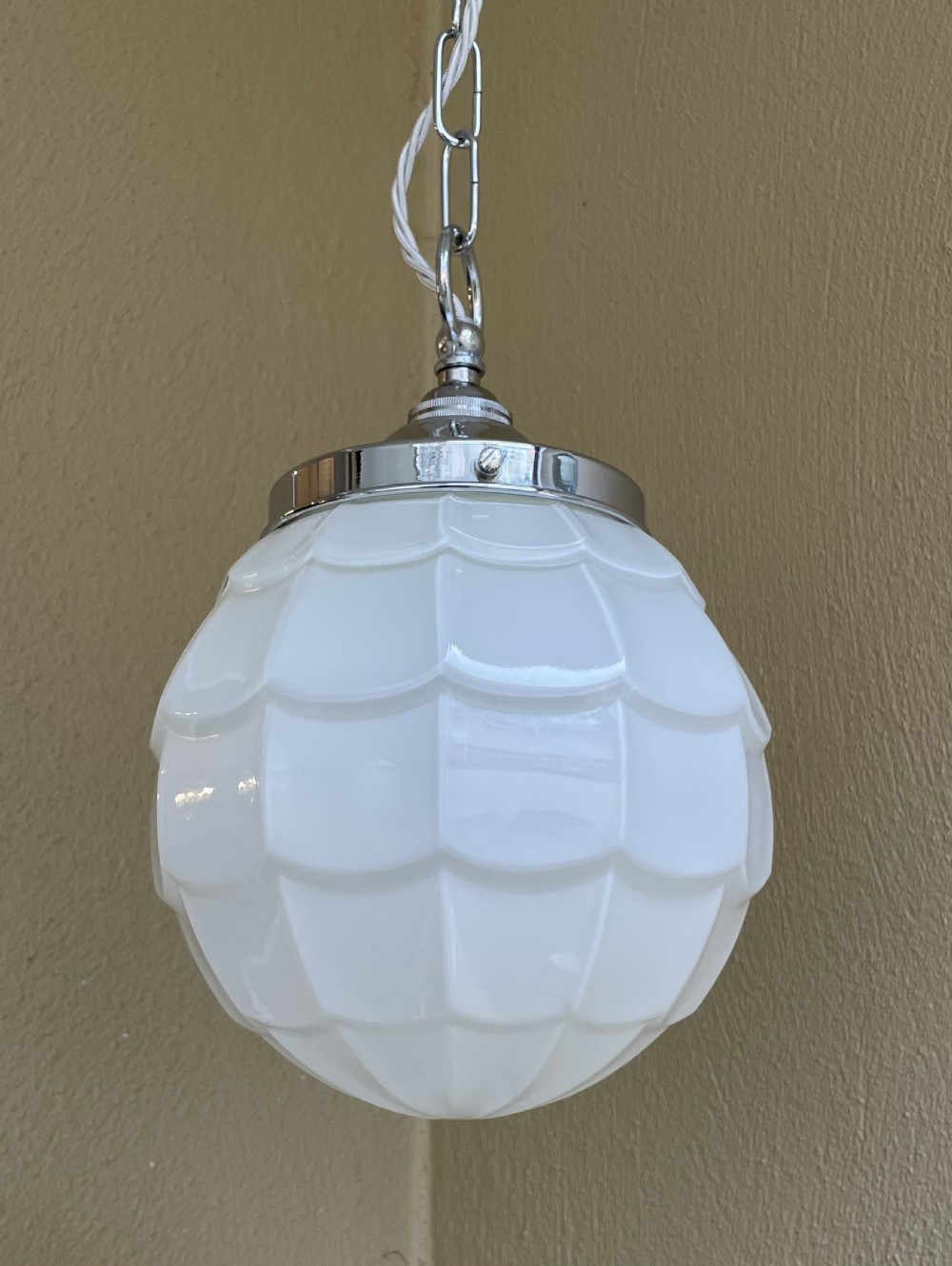 A white opaline glass spherical pendant light with a moulded fish scale texture, suspended by a chrome gallery and metal chain. View VI