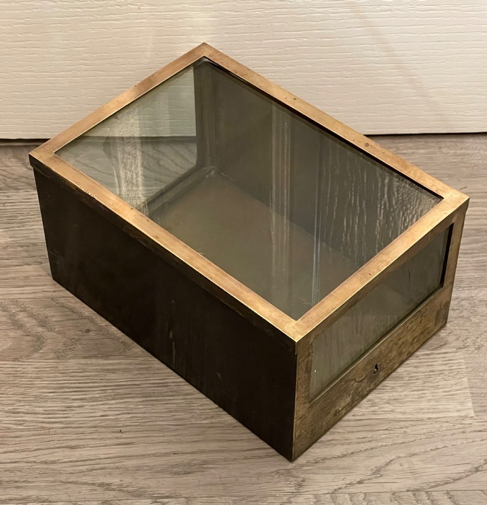A rectangular patinated brass display case featuring a clear glass top, glazed front panel, and lower brass section with a built-in keyhole.
