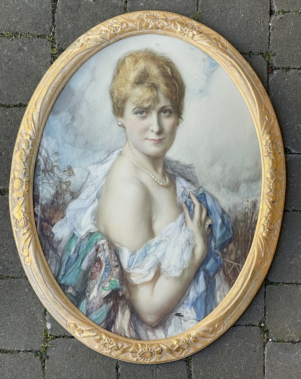 An oval watercolour portrait painting of a fair-haired woman in a light blue off-the-shoulder dress within an ornate gilded oval frame.