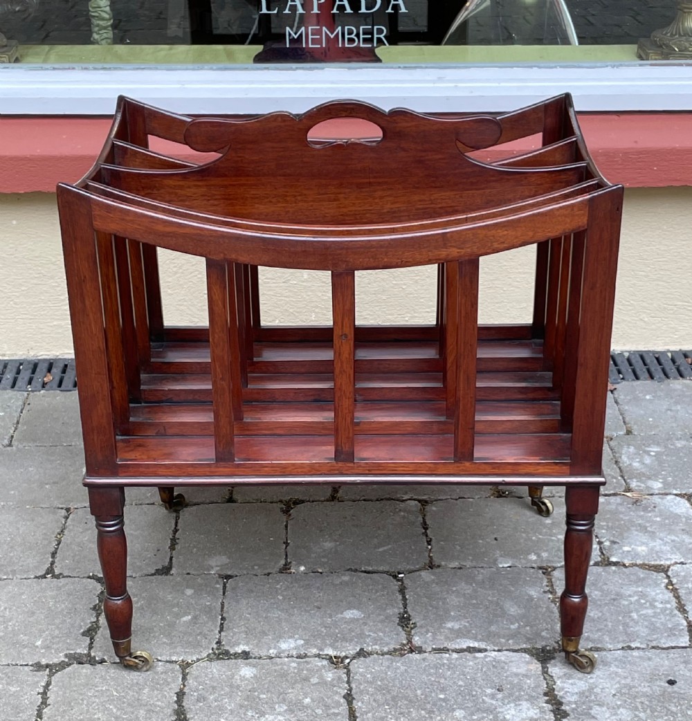 A Georgian mahogany Canterbury with slatted dividers, central cutout carrying handle, ebony inlay, and turned legs with brass castors.