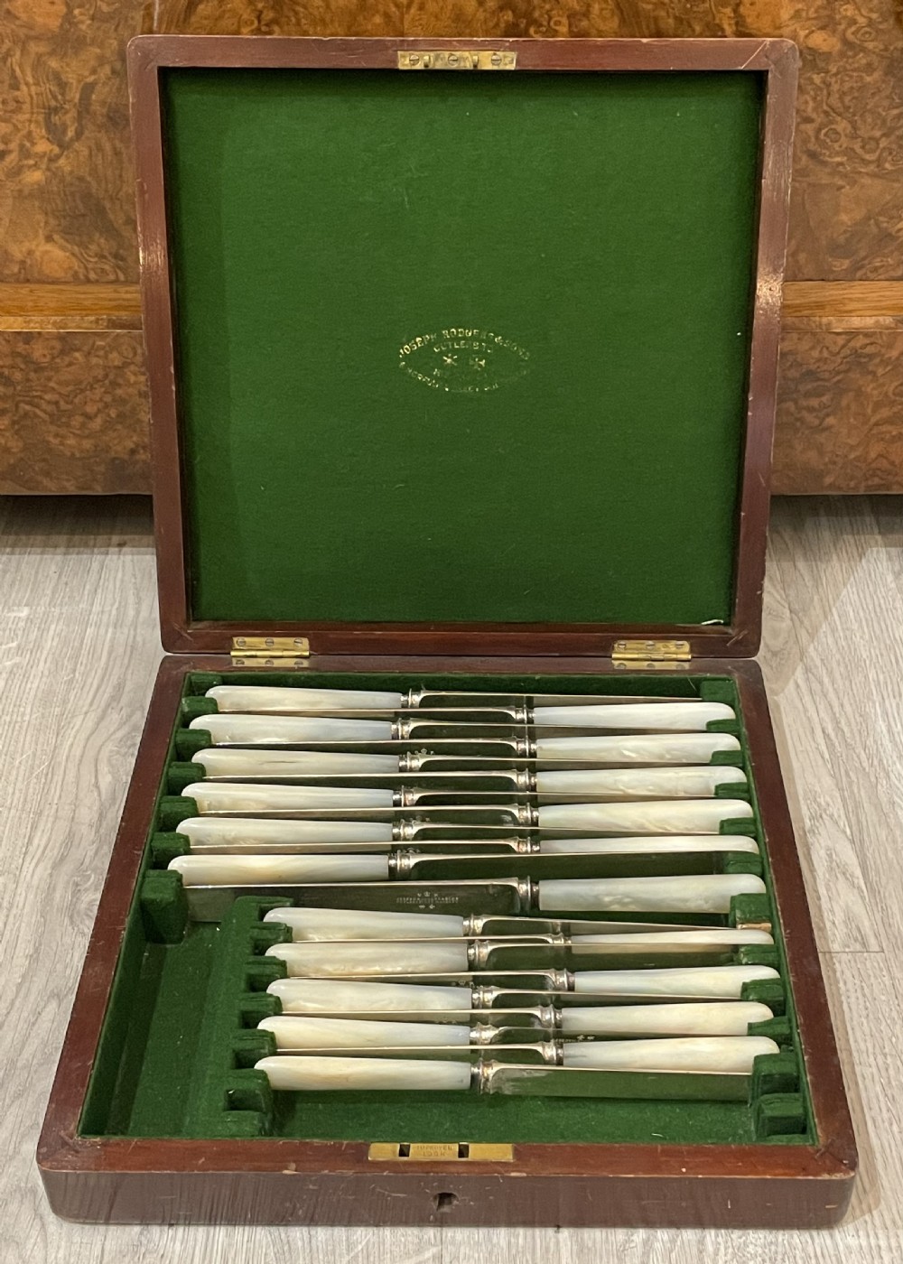 An open fitted mahogany case lined with green velvet holding steel knives with iridescent mother of pearl handles. View III
