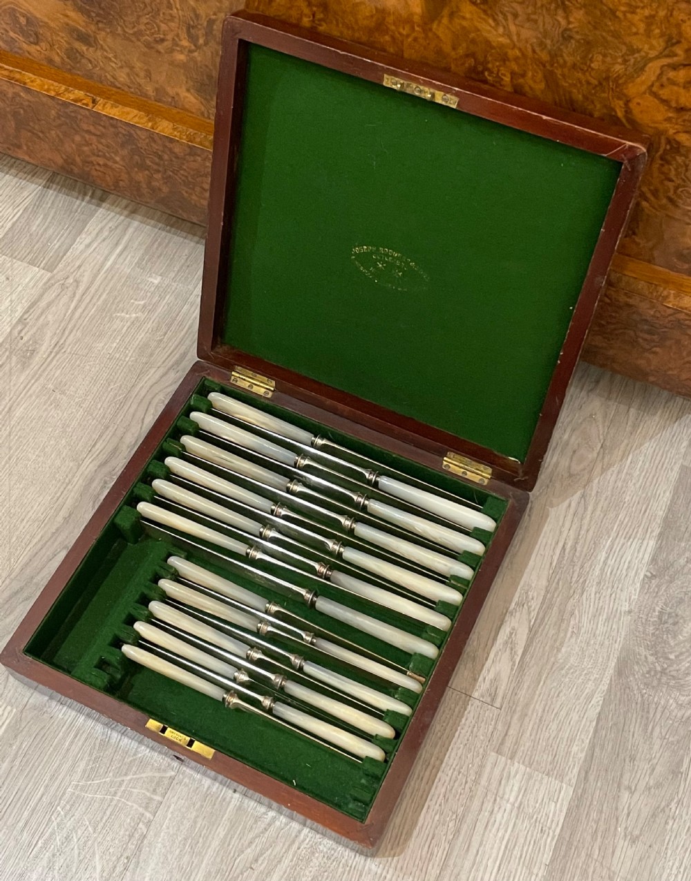 An open fitted mahogany case lined with green velvet holding steel knives with iridescent mother of pearl handles. View IV