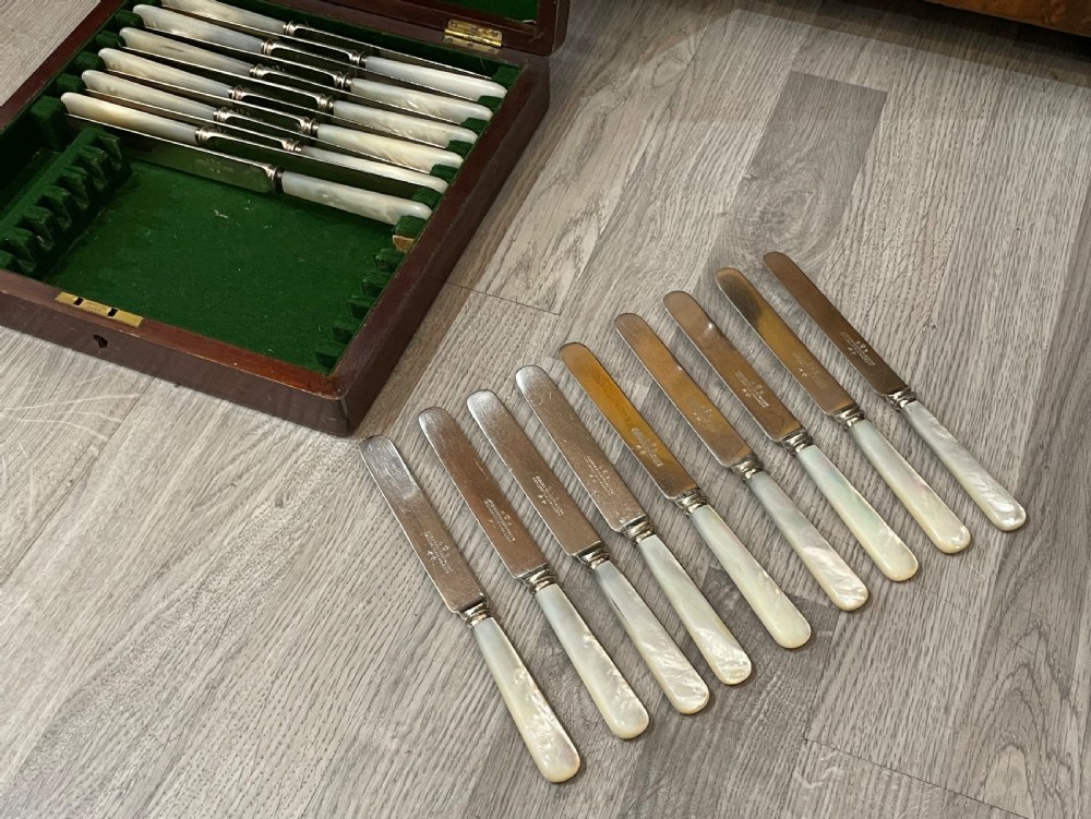 An open fitted mahogany case lined with green velvet holding steel knives with iridescent mother of pearl handles. View V