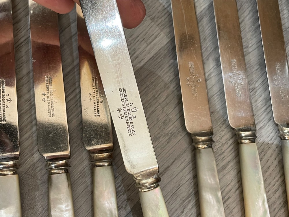 An open fitted mahogany case lined with green velvet holding steel knives with iridescent mother of pearl handles. View VI