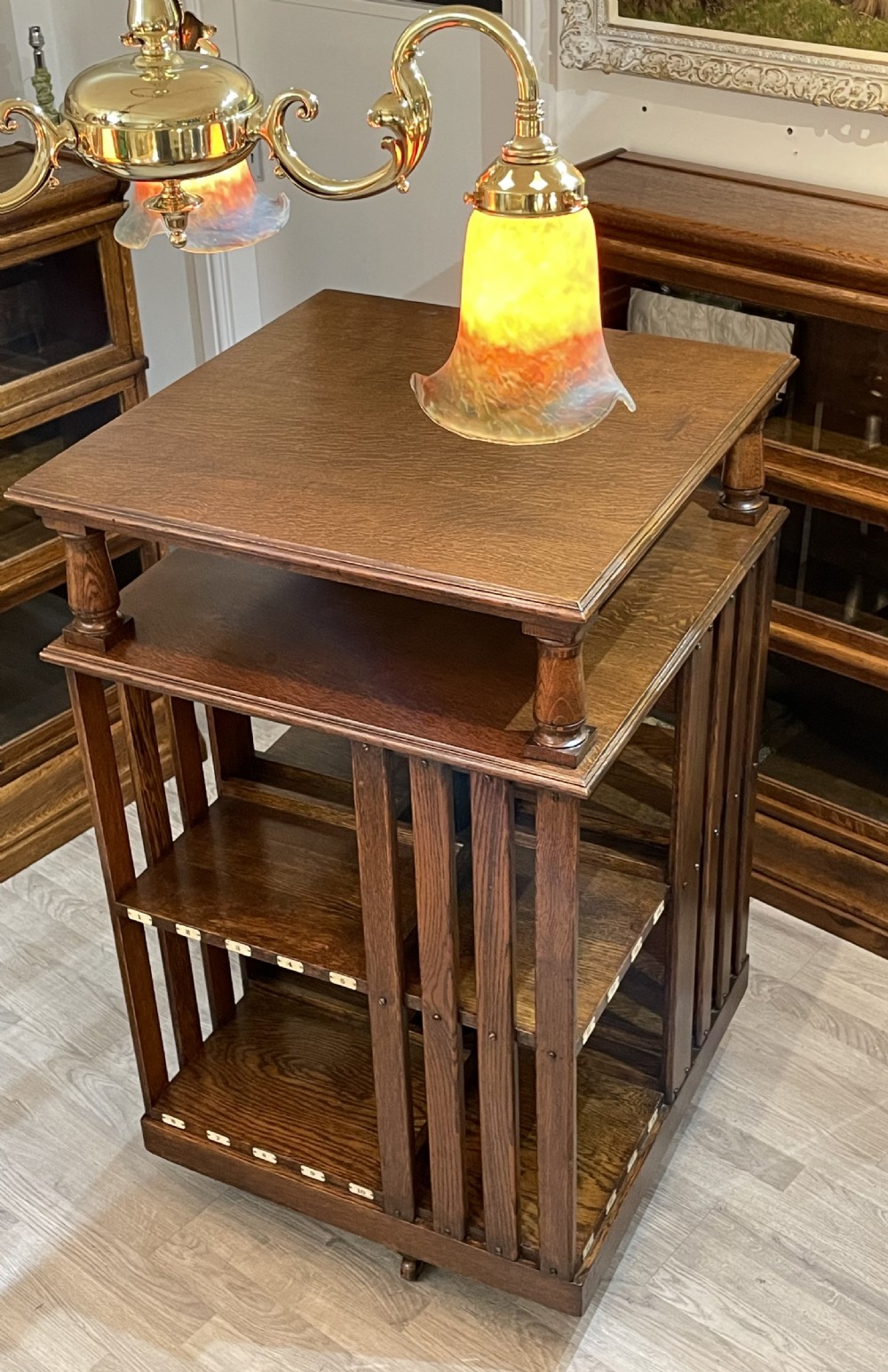A multi-tiered Edwardian dark oak revolving bookcase with vertical side slats, upper gallery spindles, and small numbered tags along the shelf edges. View II